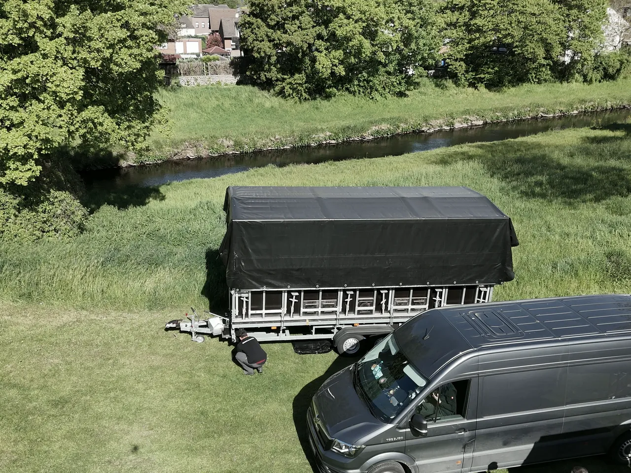 Luftbild einer aufgebauten Trailerbühne mit Transporter am Ufer eines Bachlaufs